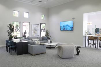A living room with a grey sofa, a black cabinet, a white coffee table, and a television mounted on the wall.
